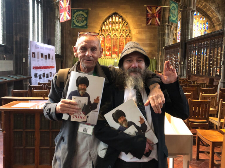 Two formerly homeless men in Manchester Cathedral holding Book of Ours.