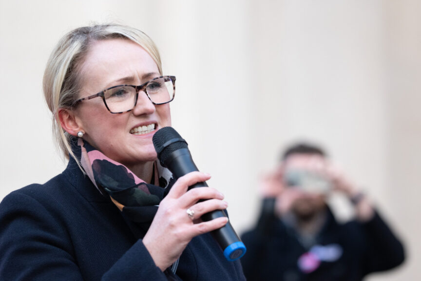 Salford MP, Rebecca Long-Bailey speaks to the crowd. She wears dark-framed glasses, and has blonde hair tied in a ponytail. She wears a dark blue coat and a patterned scarf.