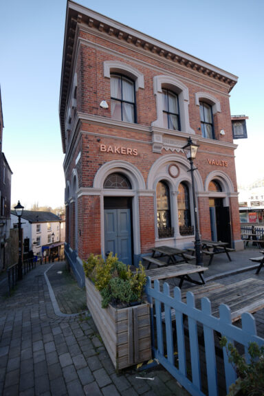 The Bakers Vaults pub in Stockport, a detached building with a small patio area out front, just off a cobbled street.