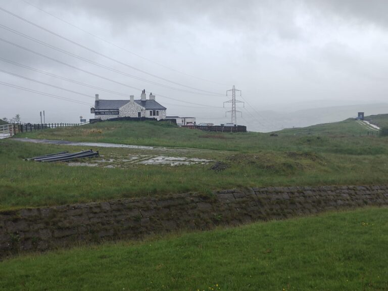 A country pub viewed from a distance. It sits on the horizon on a gloomy day over the moorland.