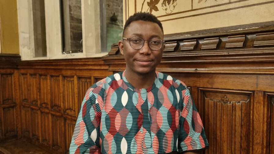 A black man with a colourful shirt, short hair and glasses, stood in the elaborate interior of Rochdale Town Hall.