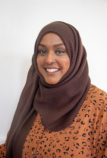 Asma is a smiling South Asian woman wearing a brown hijab and orange shirt with black animal print pattern.